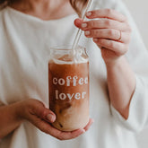 Eine Person im weißen Hemd rührt mit einem Strohhalm in einem Eulenschnitt Hohes Trinkglas "Coffee Lover", das sich perfekt für Sommer-Cocktails eignet und auf dem der Schriftzug "coffee lover" aufgedruckt ist.