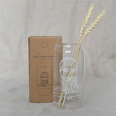 Das Hohe Trinkglas "Seemann" von Eulenschnitt ist mit einem weißen, bärtigen Matrosen illustriert und wird in einer braunen Kartonverpackung geliefert. Im Inneren des Glases befinden sich zwei getrocknete Weizenhalme, die vor einem sanften Hintergrund stehen - ideal für die Dekoration von Küstenkindern.