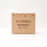 Eine braune Pappschachtel mit bunten Punkten enthält "Wachsmaler für alle" 8 Stück von Hautfarben-nachhaltige Wachsmalstifte Hautfarben für Kinder und alle, ideal zum kreativen Malen. Schachteltext: "Hautfarben Wachsmaler für Alle".