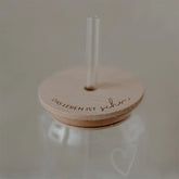 Der Eulenschnitt-Deckel "Das Leben ist schön" für Hohes Trinkglas aus FSC-zertifiziertem Buchenholz mit der Gravur "DAS LEBEN IST schön" deckt ein Klarglasgefäß mit zwei Strohhalmen ab; ein dezenter Herzumriss ziert das Gefäß.