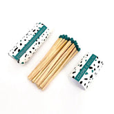 Zwei weiße Streichholzschachteln "Coudre Berlin" mit schwarzen Punkten und blaugrünen Etiketten zeigen Lange Streichhölzer - eine davon geöffnet, mit Holzstreichhölzern mit blaugrünen Spitzen und einer sichtbaren Reibfläche zum Anzünden.