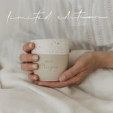 Eine Person in einem weißen, strukturierten Outfit hält den Eulenschnitt Limitierter Becher "Guten Morgen" aus Steingut; oben steht "limited edition" - eine gemütliche Szene, die sich perfekt für Geschenkideen eignet.