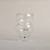 Die Eulenschnitt Double Bubble Glas "Love" Vase hat eine einzigartige Form, zeigt "LOVE" in schwarzen Buchstaben mit einem kleinen schwarzen Herz darunter und ist vor einem schlichten hellen Hintergrund fotografiert.