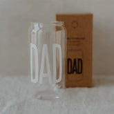 Ein hohes, klares Trinkglas "Dad" von Eulenschnitt, geformt wie eine Getränkedose und bedruckt mit dem fetten weißen Schriftzug "DAD" - perfekt als Geschenk für Papa. Präsentiert vor seiner braunen Schachtel mit Umriss und passender Aufschrift.