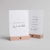 Zwei weiße Karten mit deutschen Texten stehen in Eulenschnitt Postkartenständern - "Herz" aus Buchenholz (2er Set). Die linke Karte zeigt "Das Leben ist eine Wundertüte", die rechte enthält einen längeren inspirierenden Spruch.
