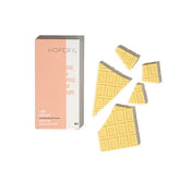 Eine teilweise ausgepackte Hopery Lime Grapefruit Badeschokolade zeigt mehrere abgebrochene Stücke neben der Verpackung auf weißem Hintergrund.