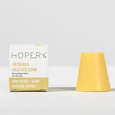 Eine Schachtel mit der Aufschrift Hopery Ultra Rich Face Serum Dry Skin steht neben einem gelben Serumblock auf einer weißen Fläche - ideal für vegane Gesichtspflege und trockene Haut - vor einem hellgrauen Hintergrund.