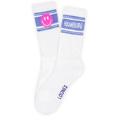 Socken "HAPPY HAMBURG | Smiley" von Loones: Weiße Hamburger Tennissocken mit blauen Streifen, pinkem Smiley auf einer Socke und "HAMBURG" auf dem anderen. LOONES-Logo an der Sohle. Aus Bio-Baumwolle für nachhaltigen Komfort.