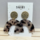 Ein Paar Shiri Ohrringe "Berlin" mit goldenen, strukturierten, runden Ohrsteckern und großen, geschwungenen, schildpattgemusterten Acetat-Anhängern, die auf einer weißen Karte mit der Aufschrift SHIRI und einem Herz über dem Text präsentiert werden.