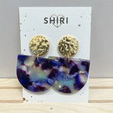 Ein Paar Shiri Ohrringe "Kopenhagen" mit gehämmerten goldfarbenen Nieten und großen marmorierten violetten, blauen und weißen Tropfen - perfekt als Statement-Schmuck in Hannover - ausgestellt auf einer Karte mit der Aufschrift SHIRI.