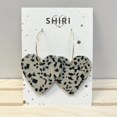 Ein Paar leichte Acetat Ohrringe "Rio" von Shiri mit großen, herzförmigen Anhängern in einem weiß-schwarz gepunkteten Muster. Ausgestellt auf einer Markenkarte mit SHIRI und einem Herzumriss. Handgemacht in Hannover.