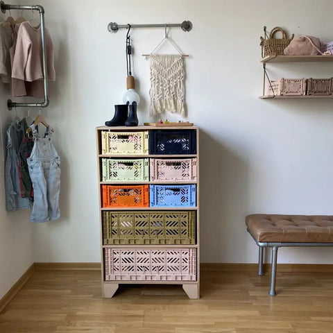 In einem aufgeräumten Raum steht ein lebendiger Schrank mit Aykasa Ay-Kasa Klappbox Midi Kisten, umgeben von hängender Kleidung, einem Wandregal mit Taschen, einer Wandlampe und einer gepolsterten Bank auf Holzboden.