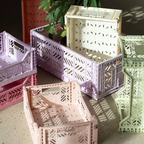 Pastellfarbene Aykasa Ay-Kasa Klappbox Midi Kisten in Rosa, Lavendel, Creme und Mintgrün sind auf einer sonnenbeschienenen Fläche gestapelt, im Hintergrund ist eine grüne Pflanze zu sehen.