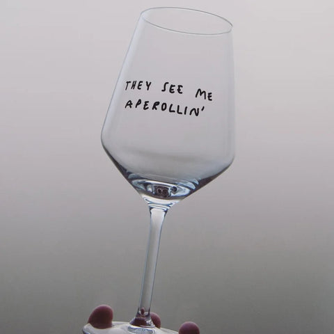Eine Hand hält das Weinglas "They See Me Aperollin'" von Johanna Schwarzer (Selekkt), das den Spruch in schwarzer Farbe auf der Schale des stilvollen Allround-Weinglases zeigt.