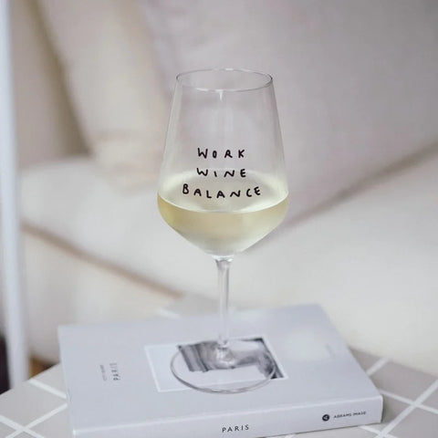 Das "Work Wine Balance" Weinglas von Johanna Schwarzer von Selekkt steht auf einem geschlossenen Buch auf dem Tisch, im Hintergrund ist eine unscharfe Couch zu sehen.