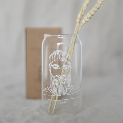 Das Eulenschnitt Hohes Trinkglas "Seemann" ist ein klares Glas mit der weißen Strichzeichnung eines bärtigen Mannes mit Hut, der Weizen in der Hand hält, und einem verschwommenen braunen Rechteck im Hintergrund.