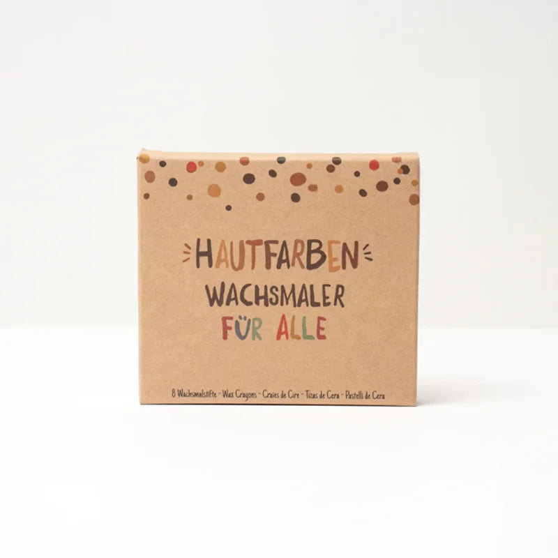 Eine braune Pappschachtel mit bunten Punkten enthält "Wachsmaler für alle" 8 Stück von Hautfarben-nachhaltige Wachsmalstifte Hautfarben für Kinder und alle, ideal zum kreativen Malen. Schachteltext: "Hautfarben Wachsmaler für Alle".
