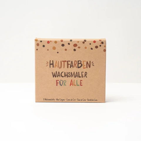 Eine braune Pappschachtel mit bunten Punkten enthält "Wachsmaler für alle" 8 Stück von Hautfarben-nachhaltige Wachsmalstifte Hautfarben für Kinder und alle, ideal zum kreativen Malen. Schachteltext: "Hautfarben Wachsmaler für Alle".