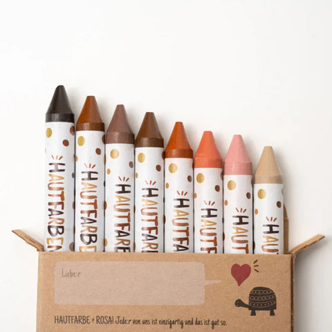 Die "Wachsmaler für alle" 8 Stück von Hautfarben sind nachhaltige Wachsmaler für Kinder in verschiedenen Hauttönen, verpackt in einer Kartonschachtel mit Herz, kleinem Schildkrötenmotiv und gepunkteten Hüllen mit deutscher Aufschrift.