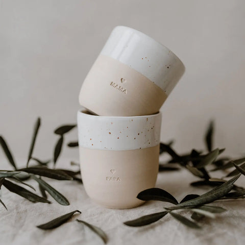 Der Becher "Mama" aus Steingut von Eulenschnitt präsentiert sich im minimalistischen Beige-Weiß-Design und ist das ideale Geschenk für Mami - stilvoll inszeniert mit Olivenzweigen auf heller, strukturierter Oberfläche.