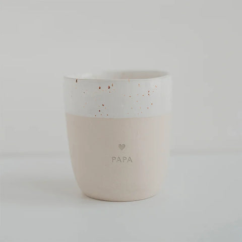 Der Steingut Becher "Papa" von Eulenschnitt hat eine weiß gesprenkelte obere Hälfte, eine hellbeige Unterseite und ist mit "PAPA" sowie einem kleinen Herz verziert. Handgemacht in Portugal.