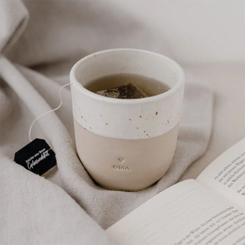Der Becher "Oma" aus Steingut von Eulenschnitt mit weiß gesprenkeltem Rand und Herz-Motiv ist das ideale Geschenk für Oma - perfekt für entspannte Momente auf der Couch mit einem guten Buch.