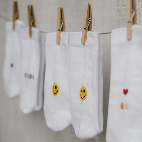 Vier Paar Eulenschnitt Socken "Smiley" gelb hängen an einer Wäscheleine mit Holzklammern. Die GOTS-zertifizierten Bio-Baumwollsocken zeigen Smiley-Motive, kleine Designs oder Text auf neutralem Hintergrund.