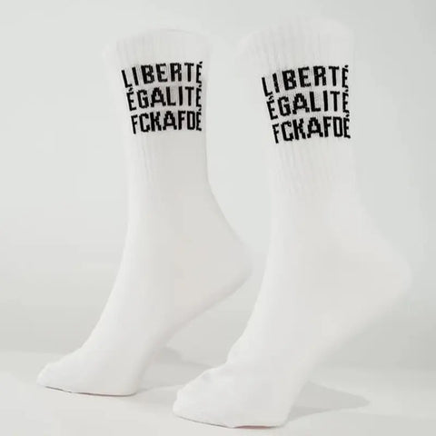 Die Arrel FCKAFDÉ Statement Socken - weiß sind aus Biobaumwolle gefertigt und mit dem schwarzen Text "LIBERTÉ ÉGALITÉ FCKAFD" versehen, der vertikal in der Nähe des oberen Randes auf einem hellen Hintergrund mit Sockenpuppen aufgedruckt ist.