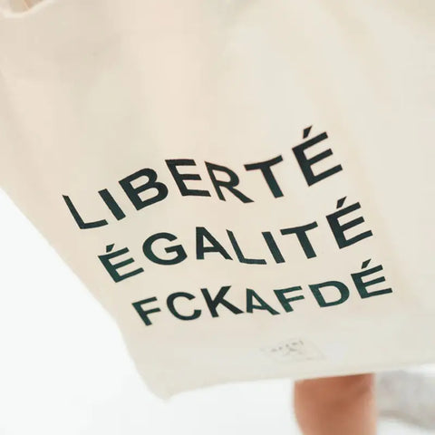 Die Arrell FCKAFDÉ Premium Tote Bag - Nature & Black zeigt einen fetten schwarzen Text auf Fairtrade-Bio-Baumwolle, der geschickt das französische Motto aufgreift und sich gleichzeitig gegen die deutsche Partei AfD stellt.