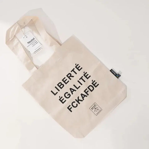 Die Arrell FCKAFDÉ Premium Tote Bag - Nature & Black ist aus fair gehandelter Bio-Baumwolle gefertigt und zeigt einen fetten schwarzen Text auf beigem Segeltuch. Ein Anhänger zum Aufhängen und ein Seitenetikett unterstreichen das ethische, stilvolle Design.