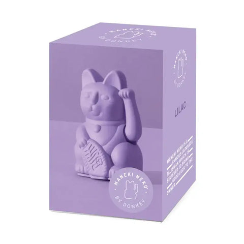 Eine lilafarbene Schachtel mit der Aufschrift "Lucky Cat - Winkekatze lila" von Donkey Products zeigt den ikonischen japanischen Glücksbringer Maneki Neko mit einer erhobenen Pfote.
