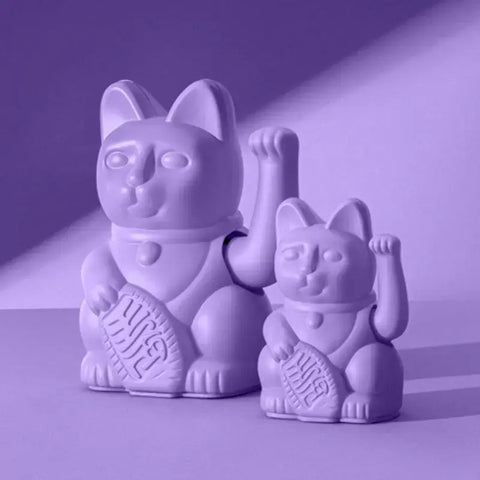 Zwei Donkey Products Lucky Cat - Winkekatze lila Figuren, eine große und eine kleine, sind nebeneinander mit erhobenen Pfoten und Münzen vor einem lila Hintergrund mit dynamischem Licht und Schatten dargestellt.