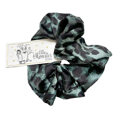 Der Leo Scrunchie von Ella & Monster hat ein schwarz-grünes Design mit einem weißen Anhänger. Es ist mit einem Mädchen und einem freundlichen Monster illustriert und ist das perfekte einzigartige Haar-Accessoire.