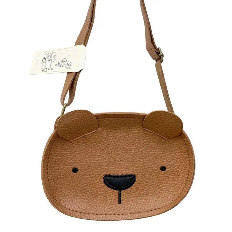 Die Tasche "Teddy" Kunstleder braun von Ella & Monster ist eine kleine braune Kindertasche in Form eines Bärengesichts mit abgerundeten Ohren, aufgenähten Augen und Nase, einem sicheren Reißverschluss und einem verstellbaren Riemen mit Anhänger.