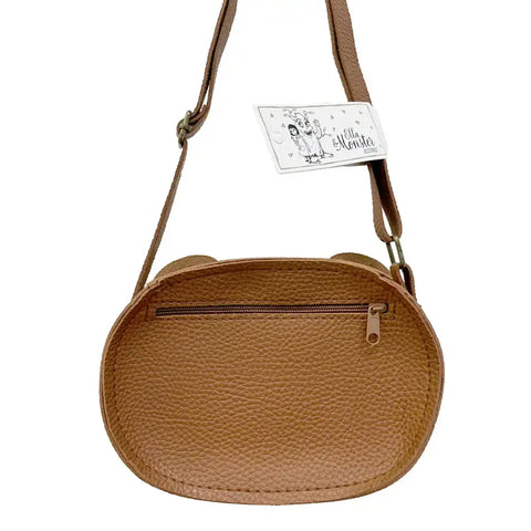 Die Tasche "Teddy" Kunstleder braun von Ella & Monster ist eine braune, strukturierte, ovale Crossbody-Tasche mit einem verstellbaren Riemen, einer Reißverschlusstasche auf der Vorderseite und einem weißen Anhänger am Riemen.