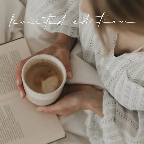 Eine Person im gestreiften Gewand hält den Eulenschnitt Limitierter Becher "Guten Morgen" aus Steingut lesend in der Hand. Oben steht in Schreibschrift "Limitierte Auflage" - ideal als Geschenkidee oder für Fans von handgefertigtem Steingut-Becher.