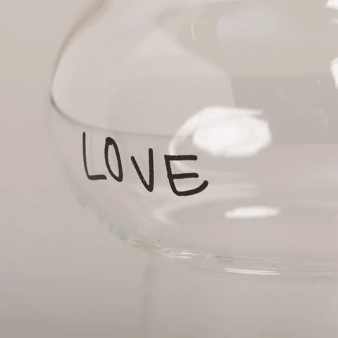Eine Nahaufnahme des Eulenschnitt Double Bubble Glas "Love" mit dem Wort LOVE in schwarzen Buchstaben auf klarem Glas. Der verschwommene, neutrale Hintergrund unterstreicht dieses romantische Trinkglas, das perfekt für besondere Momente ist.