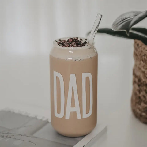Das Hohes Trinkglas "Dad" von Eulenschnitt, gefüllt mit cremigem Eiskaffee und Schokoraspeln, steht neben einer Pflanze im Korb - das ideale Geschenk für Papa.