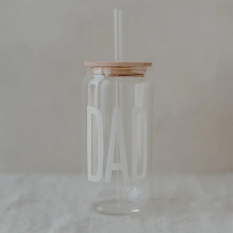 Das Eulenschnitt Hohes Trinkglas "Dad" ist ein klares Glas mit Holzdeckel und Strohhalm, das das Wort DAD in Weiß zeigt - ein ideales Geschenk für Papa, abgebildet auf einem weichen, neutralen Hintergrund.