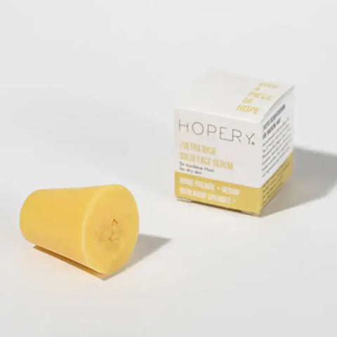 Ein festes gelbes Gesichtsserum von Hopery, Ultra Rich Face Serum Dry Skin, steht neben einer weiß-gelben Box - ideal für vegane Gesichtspflege und trockene Haut - auf schlichtem, weißem Hintergrund.
