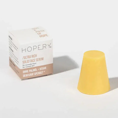 In der weiß-beigen Schachtel befindet sich ein gelbes, kegelförmiges Hopery Ultra Rich Face Serum für normale Haut, das vegane Pflege und BIO Arganöl enthält, um Ihre Haut zu nähren.