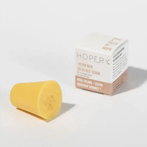 Ein gelber, fester Zylinder des Ultra Rich Face Serum Normal Skin von Hopery steht neben seiner weiß-beigen Schachtel, die die BIO Arganöl-Formel als Merkmal dieser veganen Gesichtspflege hervorhebt.