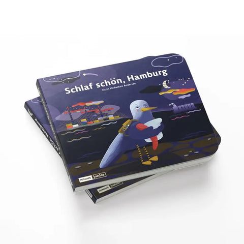 Zwei Exemplare von "Schlaf schön, Hamburg" von Karin Lindeskov Andersen (Junius Verlag) mit einem illustrierten Umschlag, der Möwe Mona, eine Möwe mit Schal, auf einem nächtlichen Kai zwischen Schiffen, Mond und Sternen zeigt.