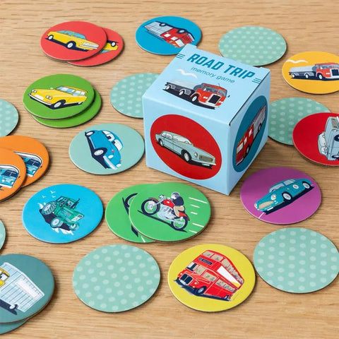 Das Memory-Spiel Road Trip (24-teilig) von Rex London wird ausgestellt, wobei bunte runde Karten mit Fahrzeugen wie Autos, Bussen, Motorrädern und Lastwagen um die zentrale Spielschachtel auf einer Holzfläche angeordnet sind.