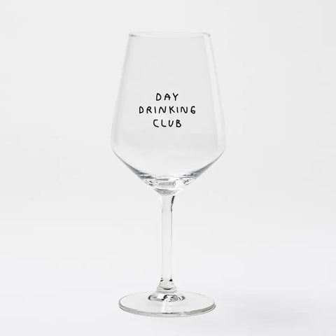 Das Weinglas "Day Drinking Club" von Johanna Schwarzer für Selekkt zeigt fette schwarze Großbuchstaben in Siebdruck auf klarem Glas vor einem schlichten weißen Hintergrund.
