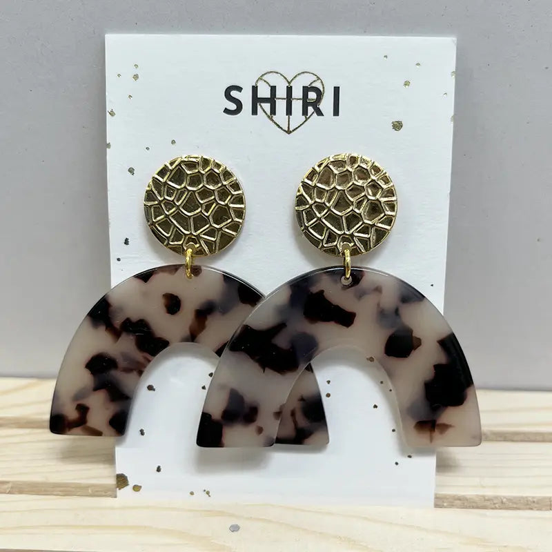Ein Paar Shiri Ohrringe "Berlin" mit goldenen, strukturierten, runden Ohrsteckern und großen, geschwungenen, schildpattgemusterten Acetat-Anhängern, die auf einer weißen Karte mit der Aufschrift SHIRI und einem Herz über dem Text präsentiert werden.