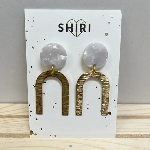 Ein Paar Shiri Ohrringe "Wien", ausgestellt auf einer SHIRI-Karte. Jeder Ohrring hat einen runden, marmorierten, weißen Ohrstecker und einen strukturierten, goldfarbenen, auf dem Kopf stehenden U-förmigen Anhänger - Statement-Schmuck aus Hannover.