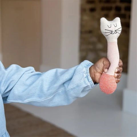 Ein Kind in einem hellblauen Langarmshirt hält die Babyrassel "Katze" Baumwolle von Sophie Home - ein weiches, sensorisches Spielzeug mit pink-beigem Körper und gesticktem Gesicht, perfekt als liebevolles Geschenk zur Geburt.