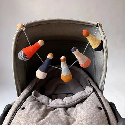 Ein grauer Kinderwagen mit einem weichen, gesteppten Innenraum, über dessen Verdeck die farbenfrohe Kinderwagenkette "Püppchen" Baumwolle von Sophie Home - Babyspielzeug in Kegelform - baumelt.