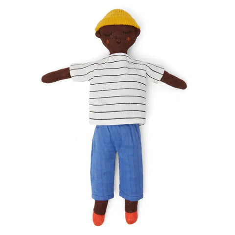 Die Sophie Home Stoffpuppe "Buddy Cobalt" Baumwolle hat dunkelbraunes Fell, eine gelbe Strickmütze, ein weiß-schwarz gestreiftes Hemd, eine blaue Hose und rote Socken. Sie liegt flach auf einem weißen Hintergrund.